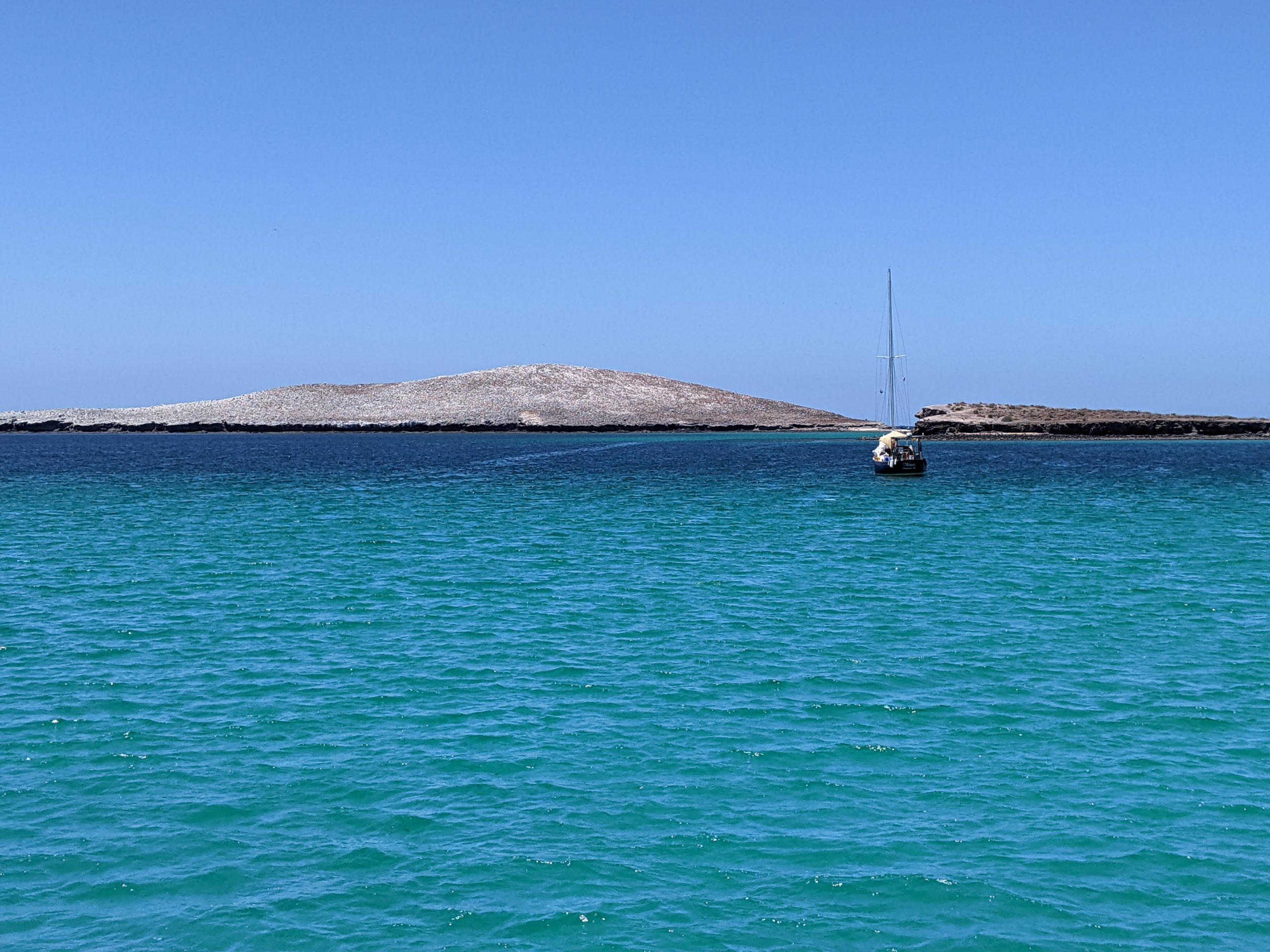 A boat drifts on a turquoise sea with land peeking up behind it