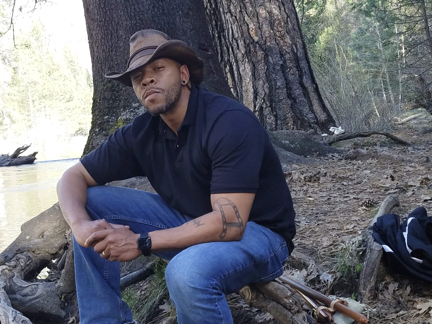 A Black man wearing a cowboy hat sits outside