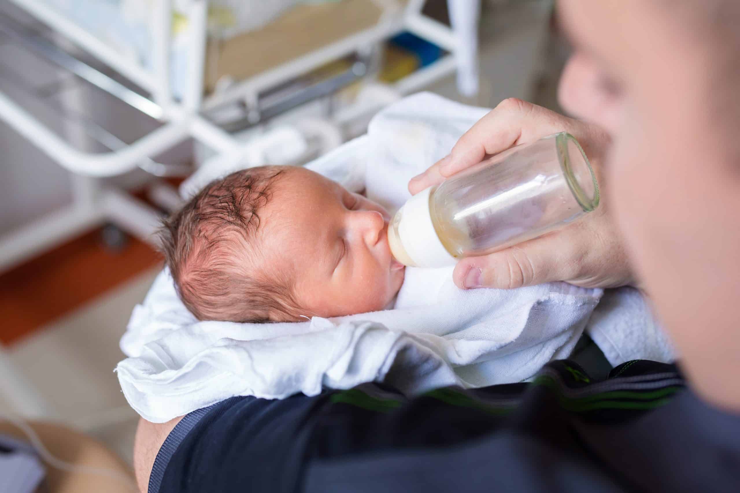 A parent feeds a baby a bottle in a hospital setting
