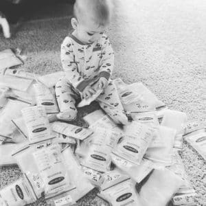 A baby sits on the floor, surrounded by small, transparent bags of breastmilk
