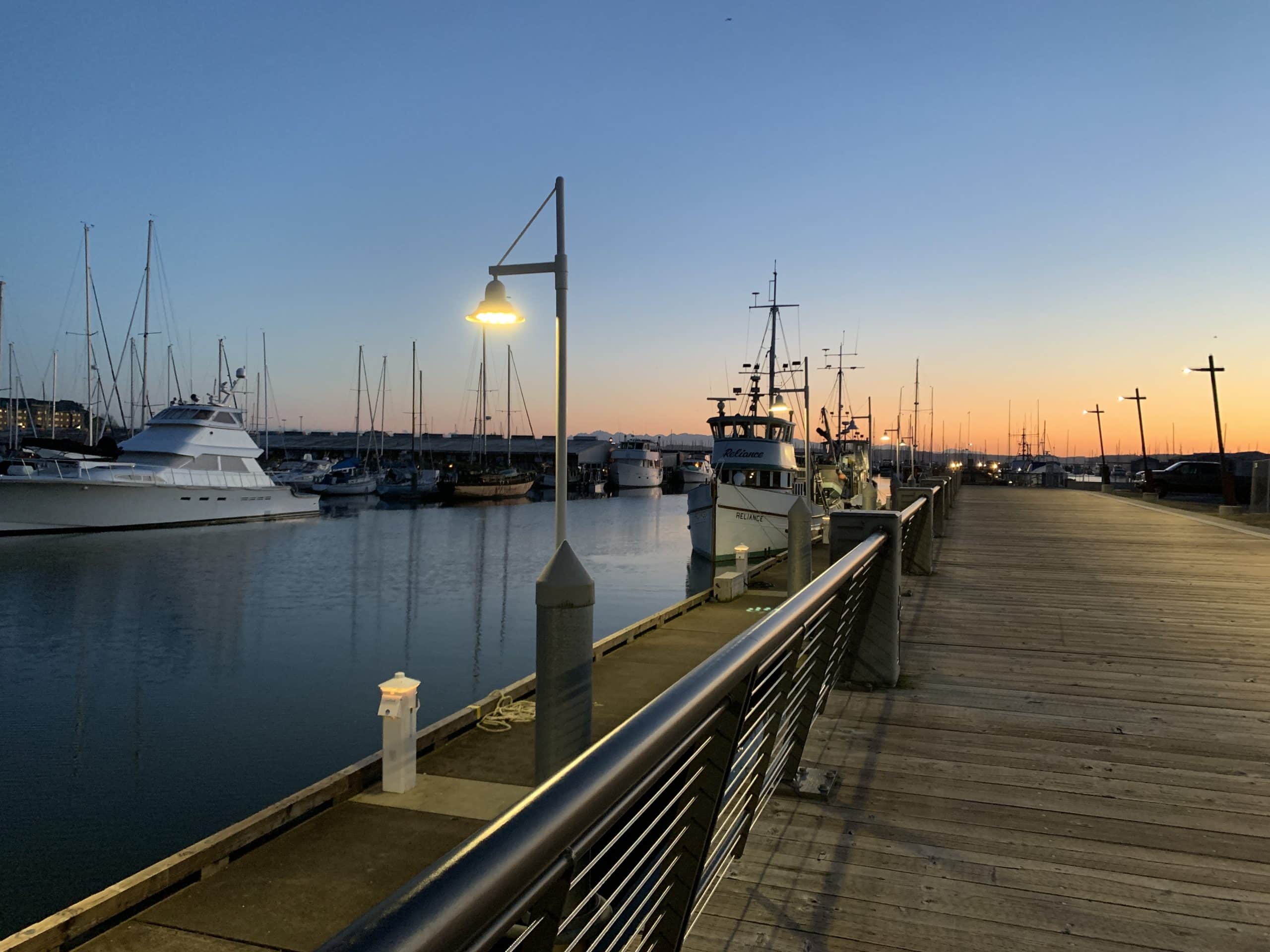 Boats sit on the Port of Everett marina around sunset with a boardwalk along the side