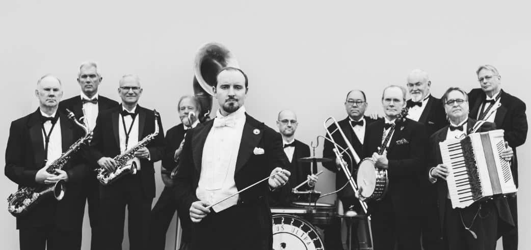 11 men stand in suits holding various big band instruments