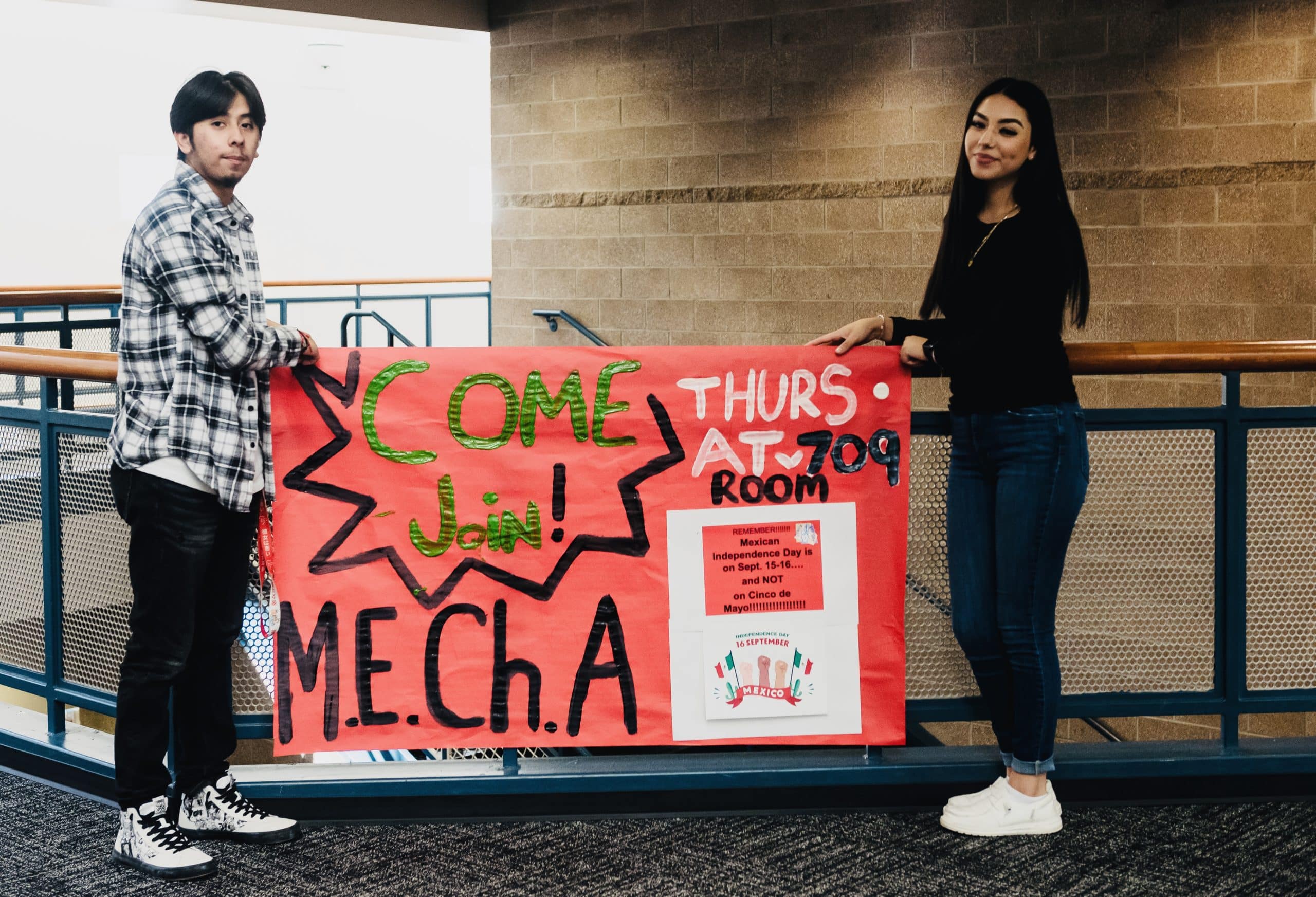 Two teens hold up a sign that says Come join M.E.Ch.A.