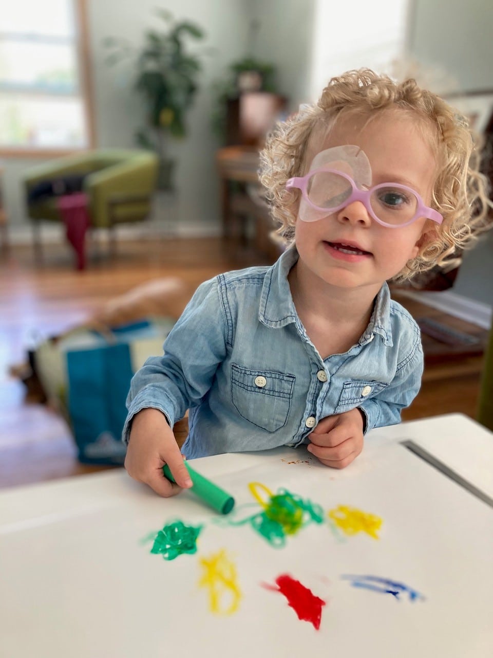 A young child with glasses and a patch over one eye plays with toys at a table