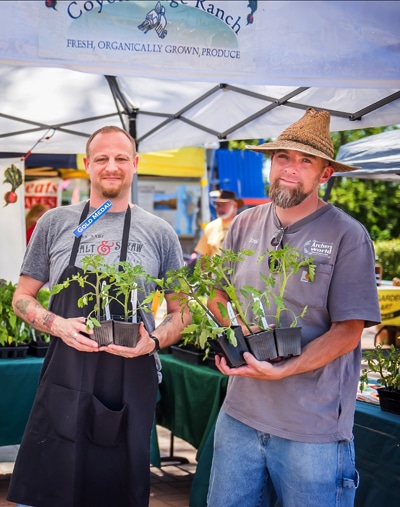 Two men smile while holding plant sprouts