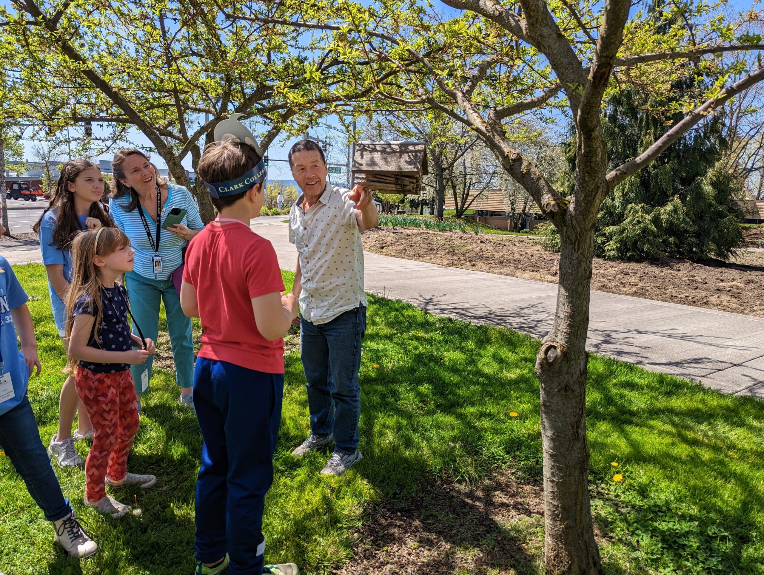 A man points to a tree while instructing several other people outdoors