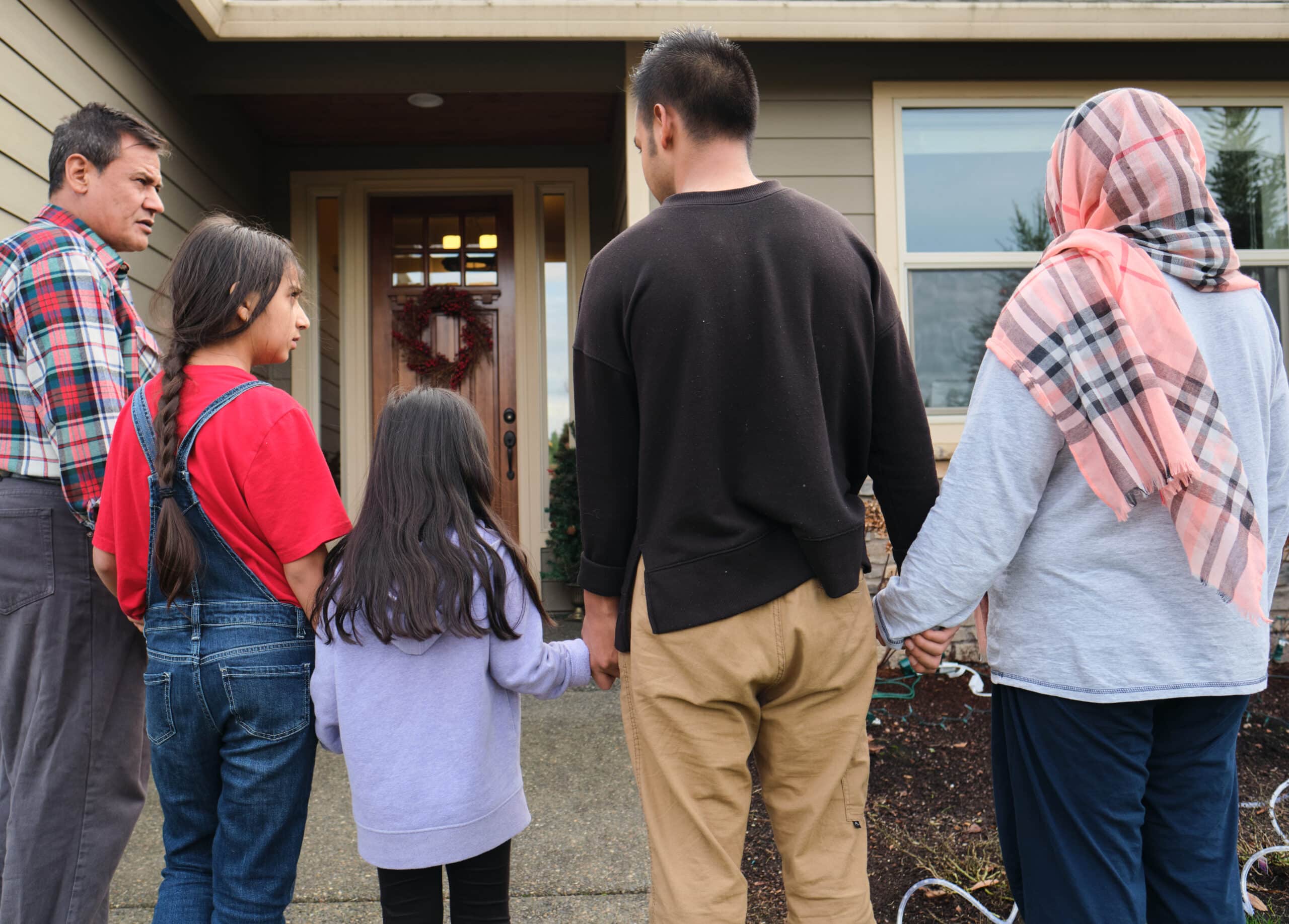 A family stands hand in hand outside the entrance to a home