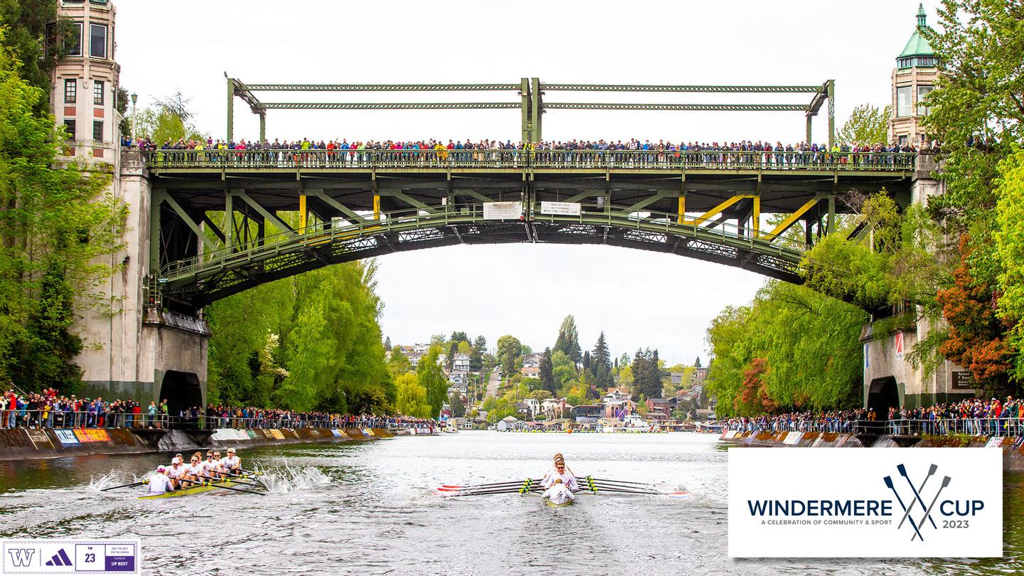 Crowds of people stand on a bridge overlooking crew teams rowing on a river
