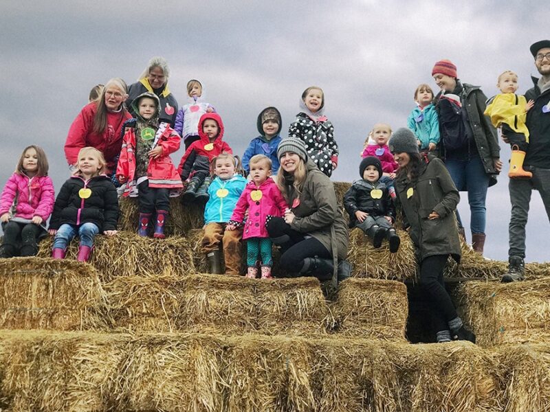 A group of parents and preschoolers stand on top of a large hay bale tower