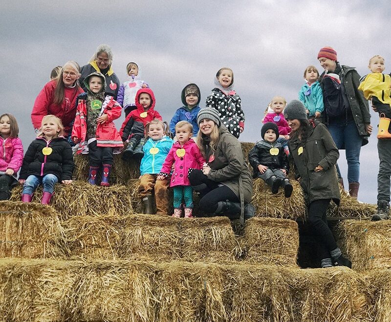 A group of parents and preschoolers stand on top of a large hay bale tower