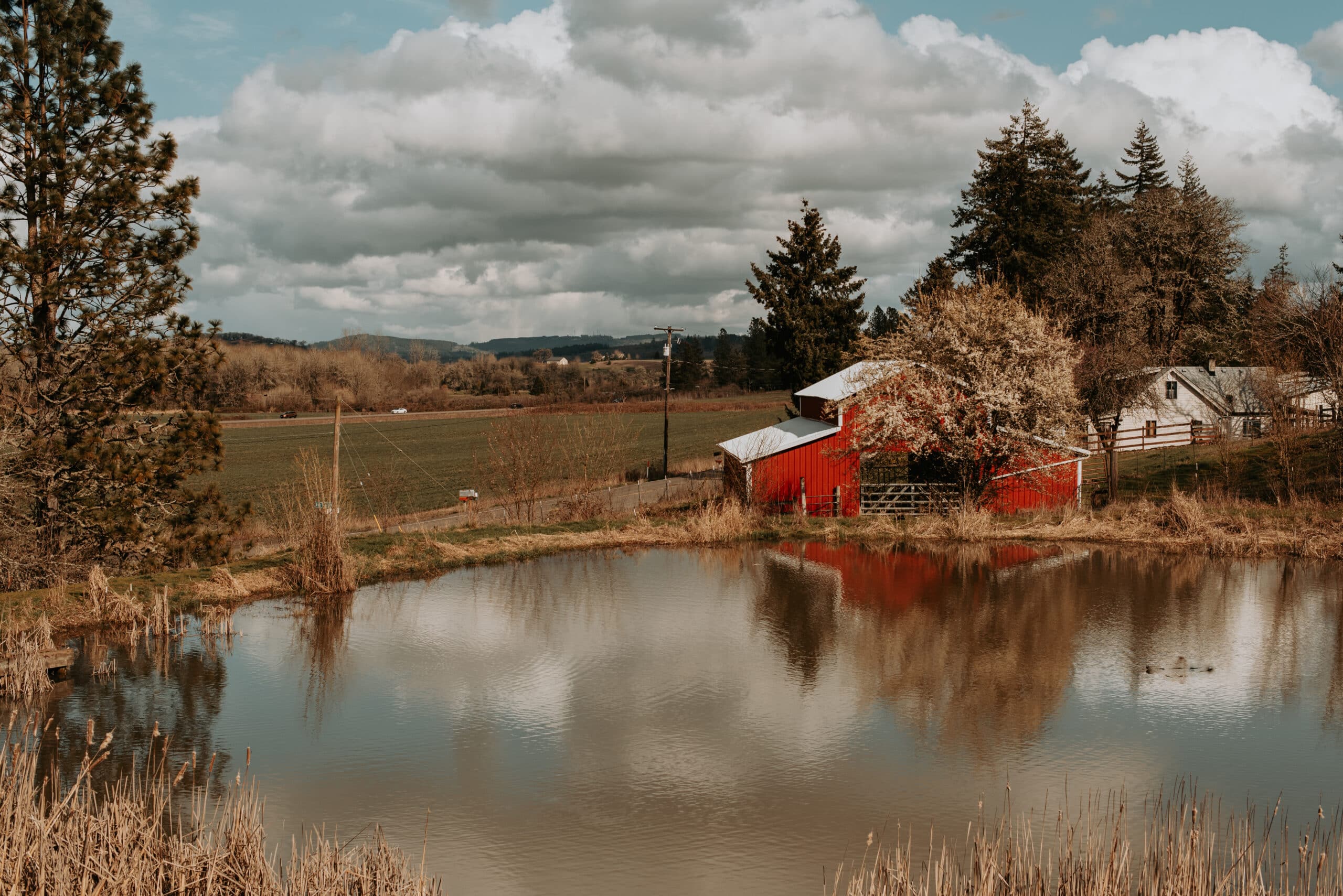 A red barn stands close to a small pond with a wide countryside all around