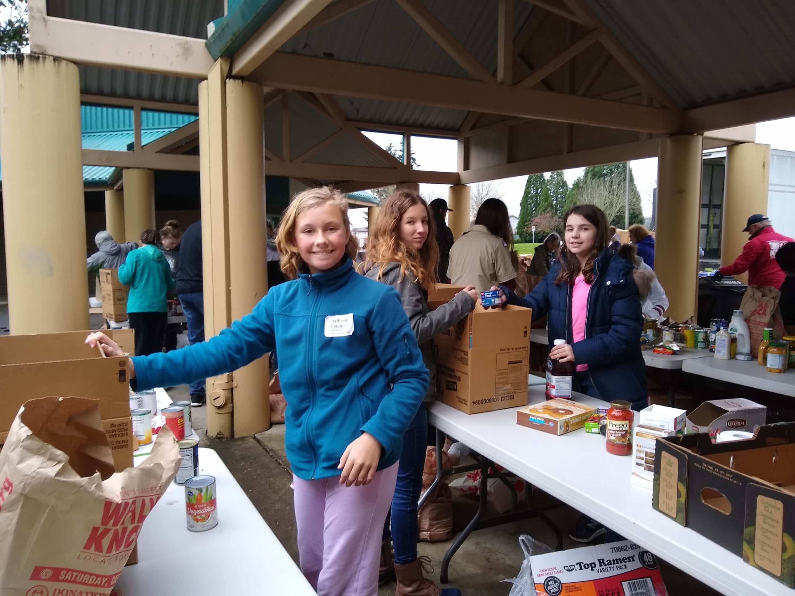Tween girls help sort non-perishable food items under a pavilion