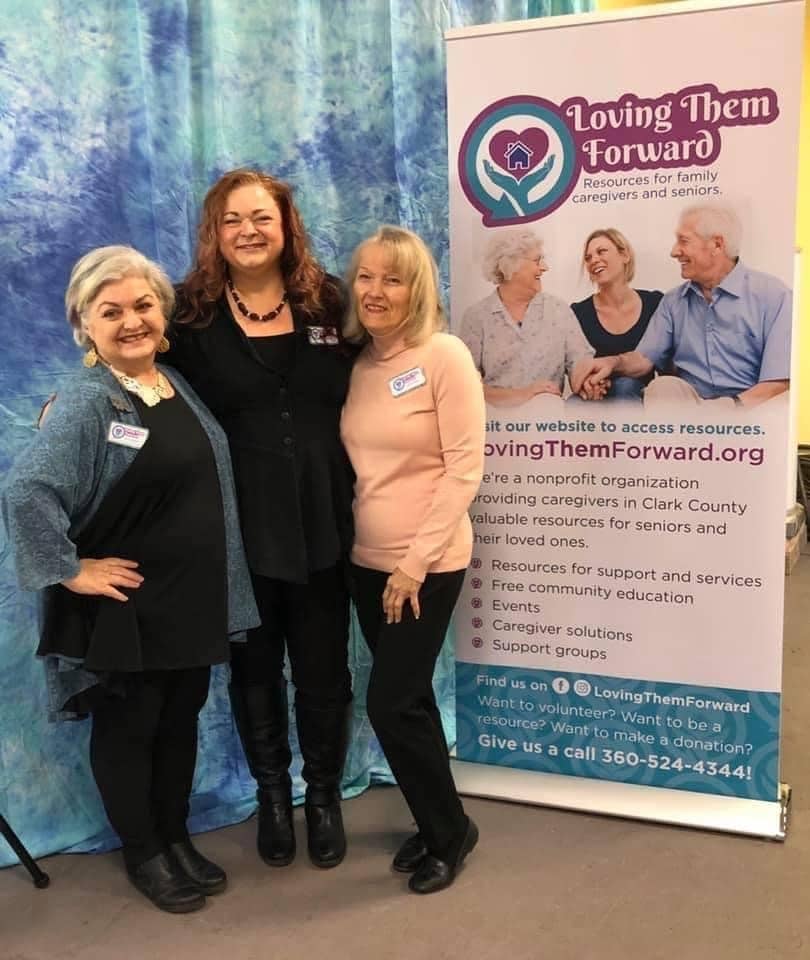 The founders of Loving Them Forward post in front of a sign at an event. The organization puts on A Caregiver Christmas each year to support caregivers in Clark County.