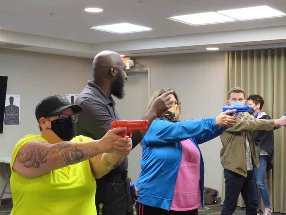 A Black man teaches a firearms safety class with participants using blue practice guns