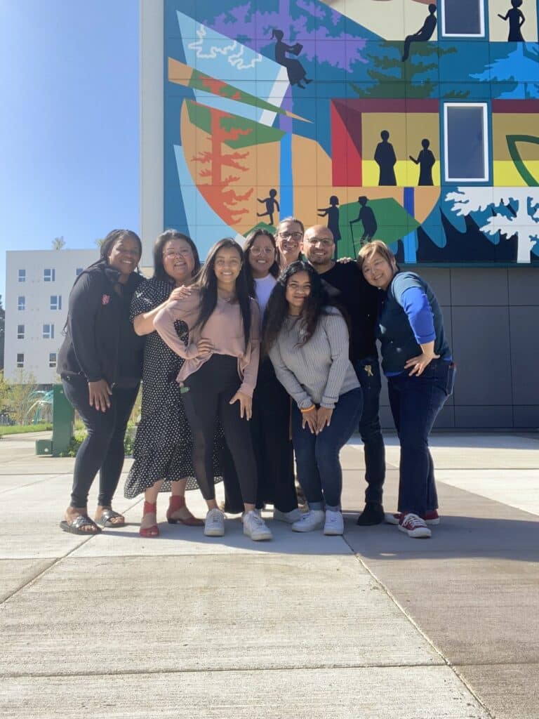 A group of people stands and smiles in front of a colorful building