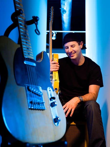 A man sits and smiles behind a guitar