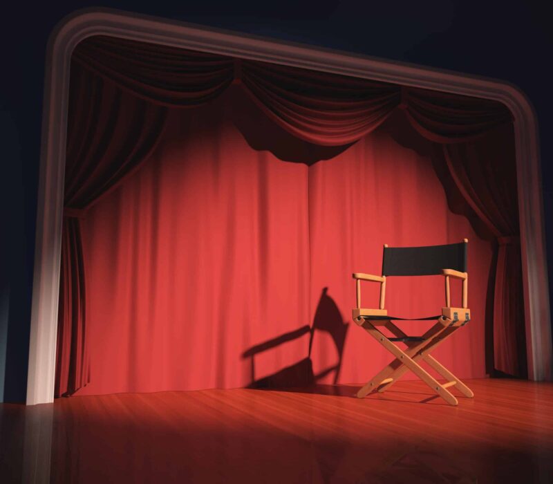 A directors chair on a stage with a red curtain behind it