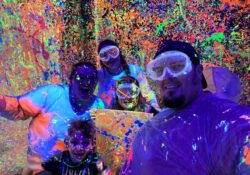 A family of 5 poses in a room with neon paint splattered everywhere