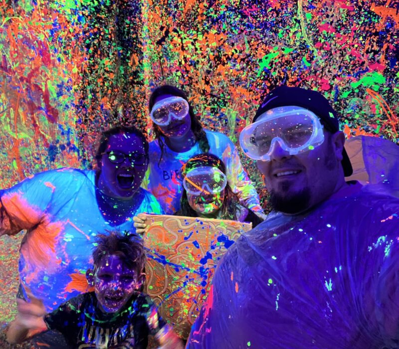 A family of 5 poses in a room with neon paint splattered everywhere