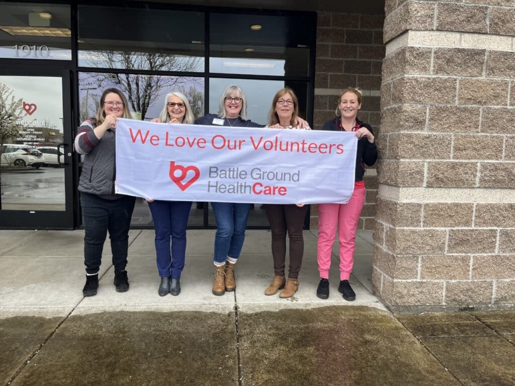 5 women at Battle Ground Health Care hold up a sign that says "We Love Our Volunteers"