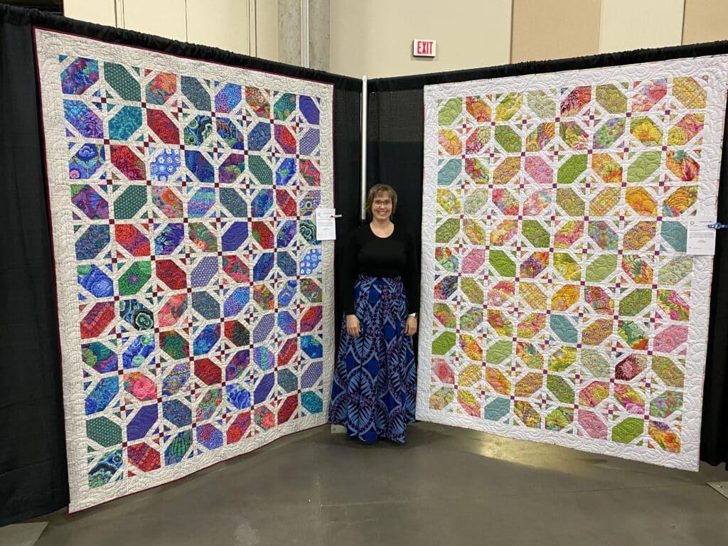 A woman poses with two large intricate quilts