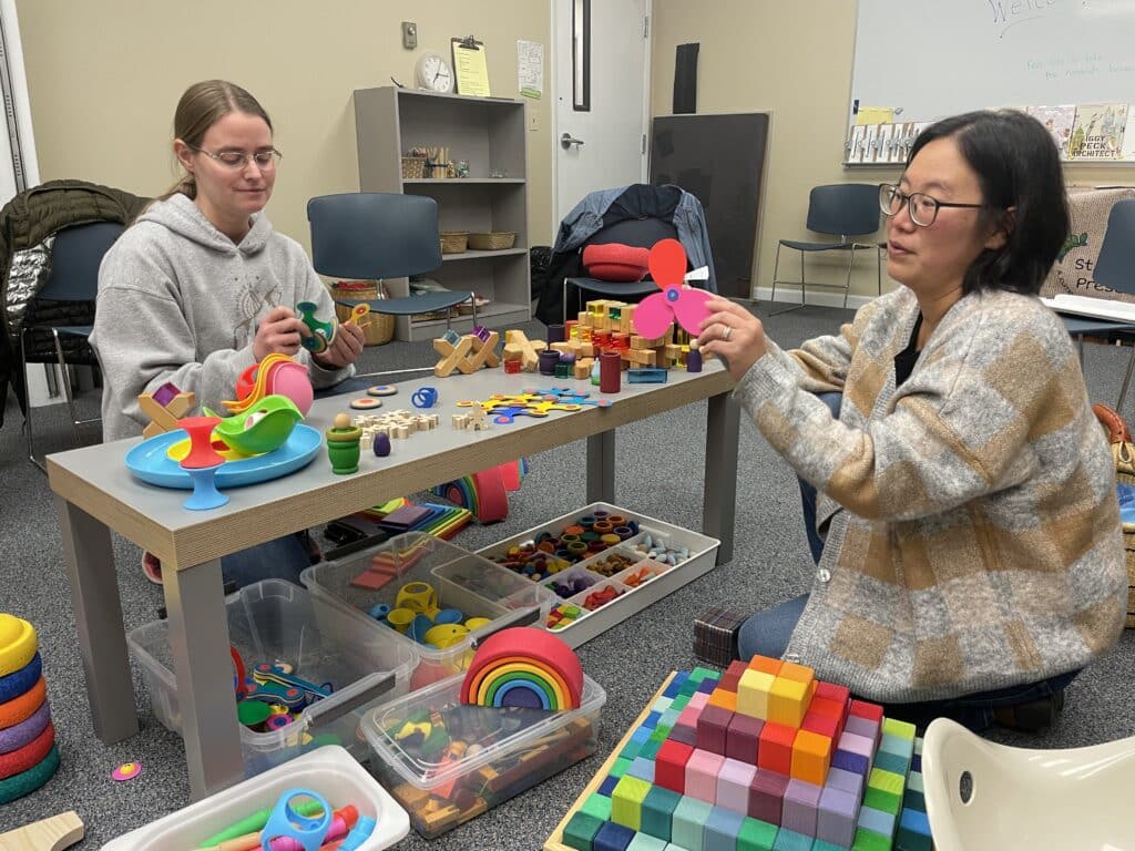 Two women play with colorful toys inside a preschool setting